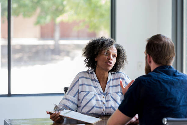 Serious mature female counselor gestures while having a conversation with a young man.